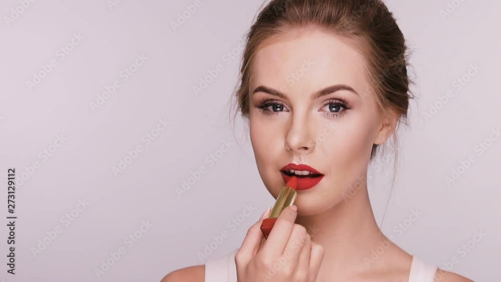 attractive woman applies red lipstick and smiles isolated on grey attractive woman applies red lipstick and smiles isolated on grey