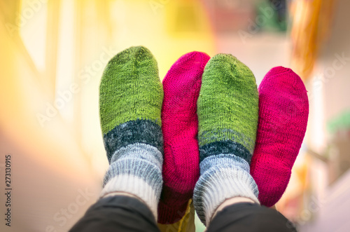 Couple in Colorful Woolen Knitted Socks Touching Each Other Feet up in the Air. People Relaxing At Home in Cold Season. Christmas, New Year, Love, Relationship, Cozy Home Concept.