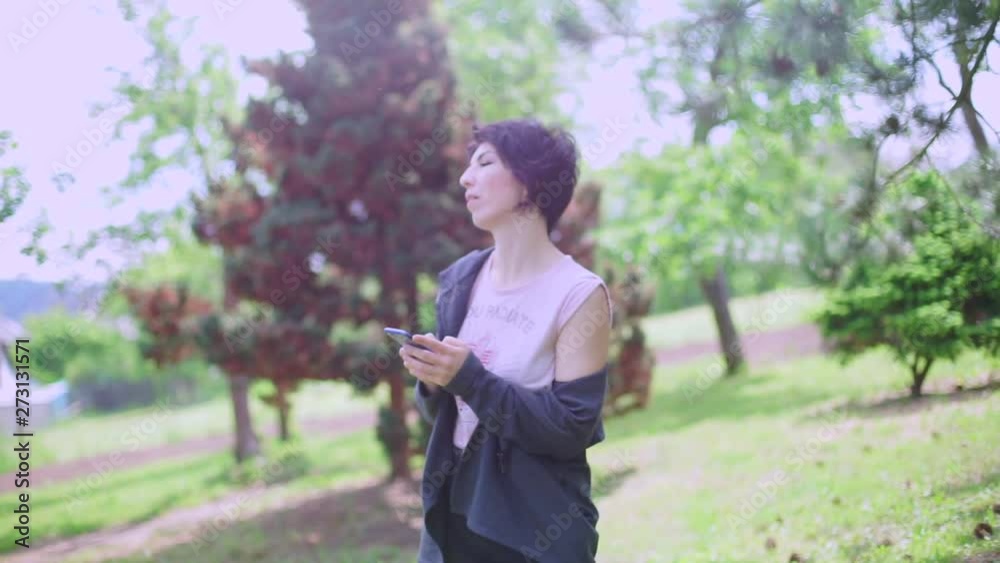 girl typing a message in the smartphone, standing in the forest girl typing a message in the smartphone, standing in the forest