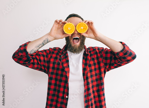 Portrait handsome young bearded man holding slices of orange in front of his eyes.