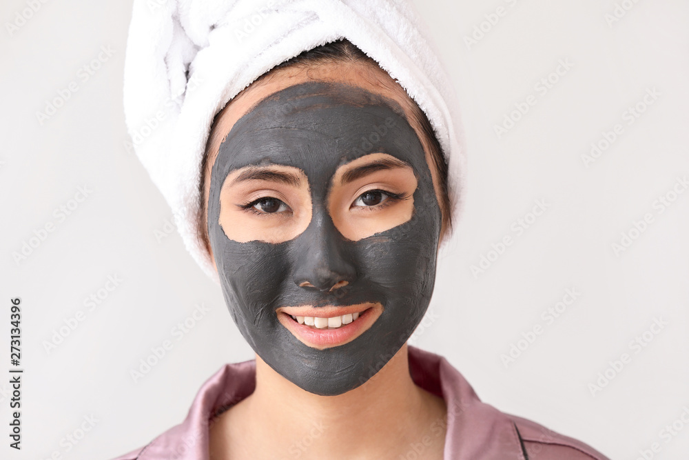 Beautiful Asian woman with facial mask on light background