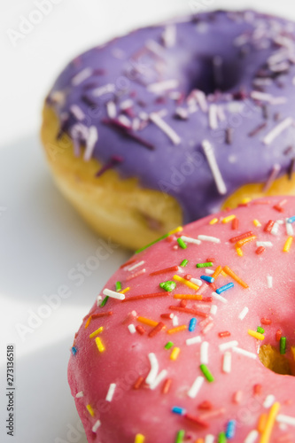 Pink and purple donuts with colorful sprinkle on white backdrop