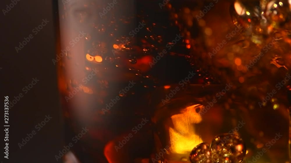 Coke with ice cubes closeup. Glass of fizzy cola rotated over brown background. Slow motion 4K UHD video footage. 3840X2160