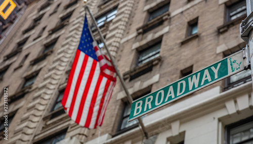 Broadway road sign. Blur American flag and buildings facade background, Manhattan downtown