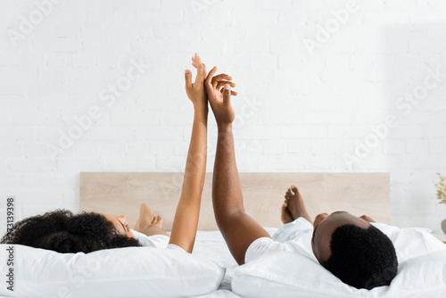 Slika na platnu happy african american man touching hands with girlfriend, lying on white bed in