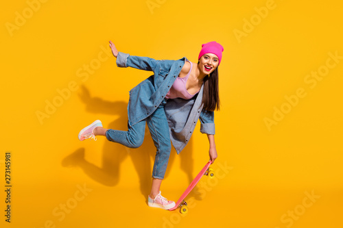 Full length side profile body size photo beautiful she her lady hand arm skate board dangerous sport movement wear casual jeans denim jacket shoes pink hat isolated yellow vivid bright background