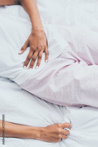 cropped view of african american woman suffering from abdominal pain while lying in bed