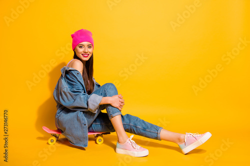 Full length side profile body size photo beautiful she her lady weekend vacation sporty free time sitting own skate board wear casual jeans denim jacket shoes pink hat isolated yellow vivid background © deagreez