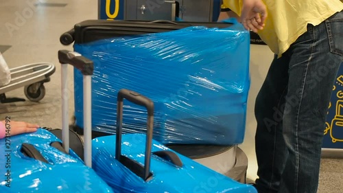 Luggage wrapping service at the airport, suitcase is packed in cellophane cling film. Workers wrapped luggage in plastic photo