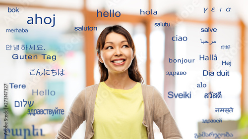 translation, education and people concept - happy asian young woman looking up over greeting words in different foreign languages