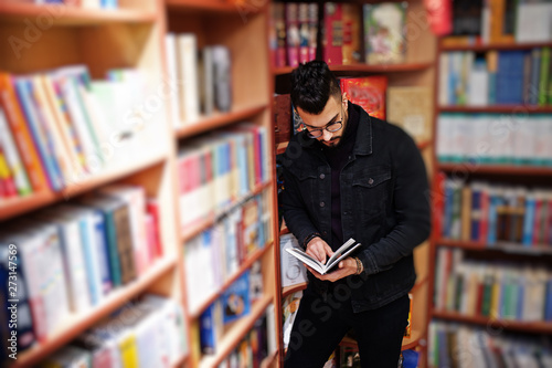 Tall smart arab student man, wear on black jeans jacket and eyeglasses, at library with book at hands.