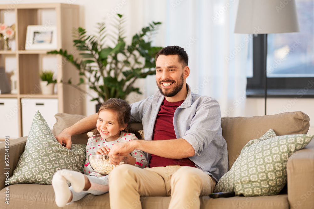 family, fatherhood and people concept - happy father and daughter with popcorn watching tv at home