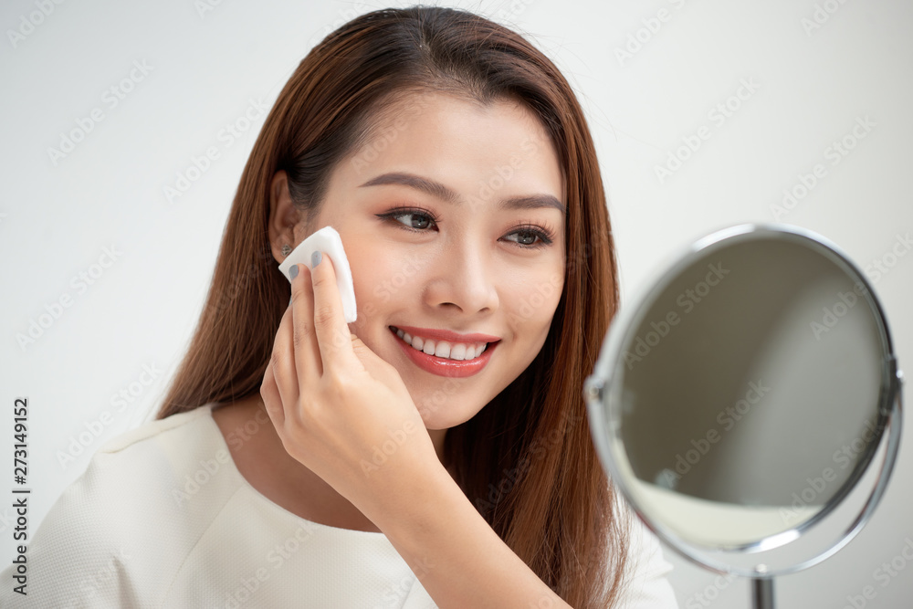 Taking off her make-up. Beautiful cheerful young woman using cotton disk and looking at her reflection in mirror with smile while sitting at the dressing table Taking off her make-up. Beautiful cheerful young woman using cotton disk and looking at her reflection in mirror with smile while sitting at the dressing table
