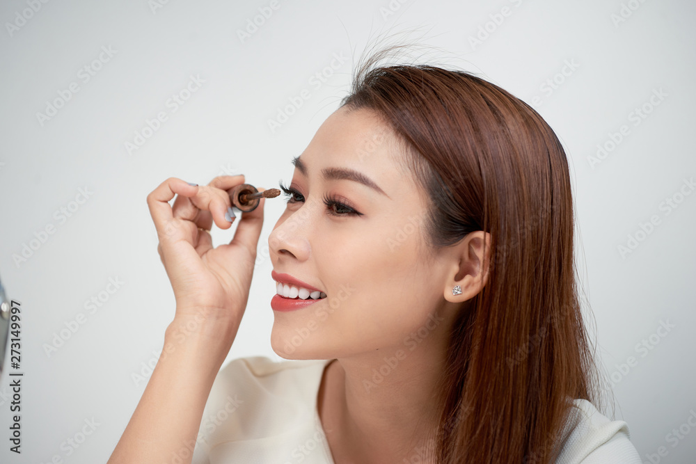 Beauty model teenage girl looking in the mirror and applying mascara make up. Beautiful young woman apply makeup Beauty model teenage girl looking in the mirror and applying mascara make up. Beautiful young woman apply makeup