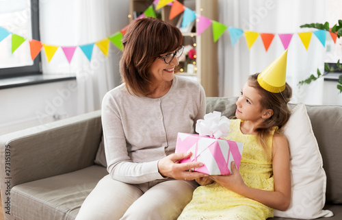 family, greetings and celebration concept - happy grandmother giving her granddaughter birthday gift at home