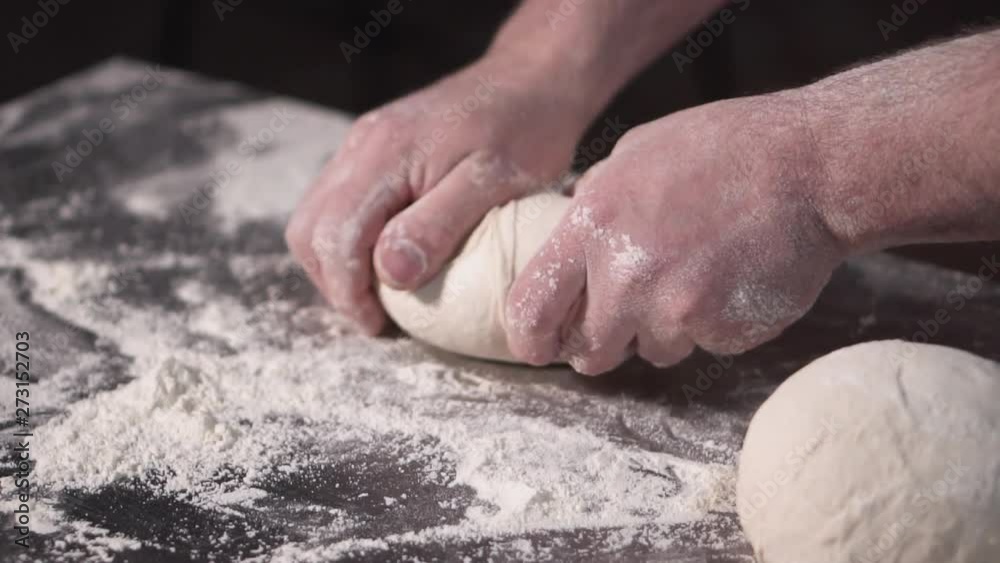 Close up view of bakers hands kneading the dough on the table. Manufacturing process, making bread . Slow motion .