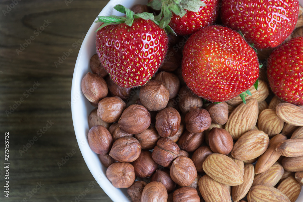 Plate of fresh strawberreis and almond, hazelnut on wooden background. Vegetarian breakfast