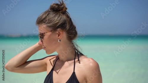 Close up portrait of beautiful young woman running hand through hair blowing in wind on tropical beach slow motion