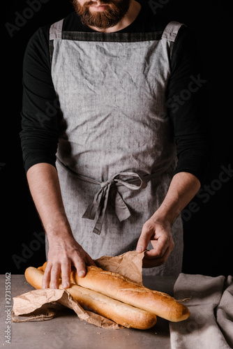 The man opened the packed baguettes on the table. Black background.