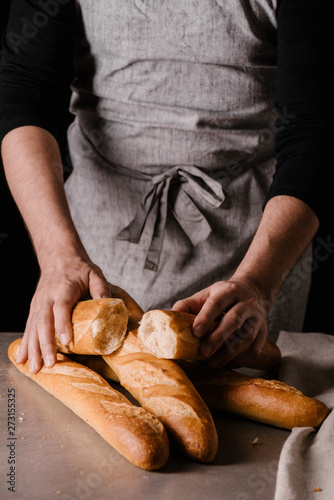Male hands hold the halves of a baguette and three freshly baked baguettes on the table. Black background.