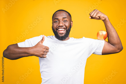 Healthy african american man holding an apple isolated against yellow background.