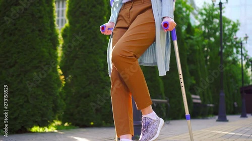 unrecognizable disabled woman with an injury on crutches walking in the Park Sunny slow mo