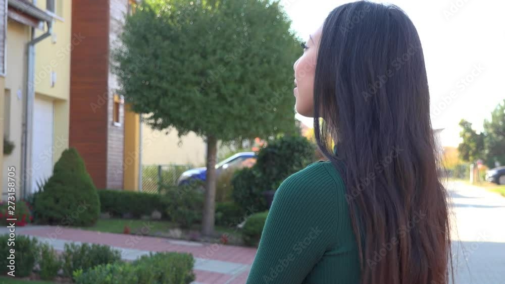 An Asian woman looks around a suburban area with a smile