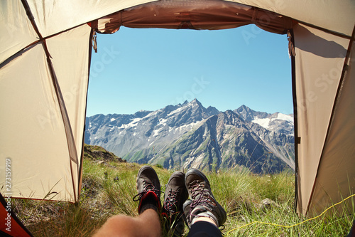 Two pairs of legs in hiking tourist boots at exit of tent