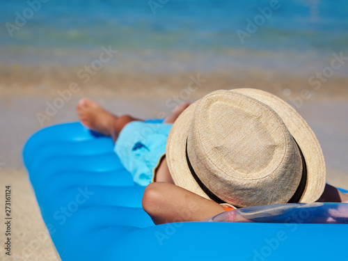 European boy in a sun hat enjoying the serenity of ocean laying on the air mattress.