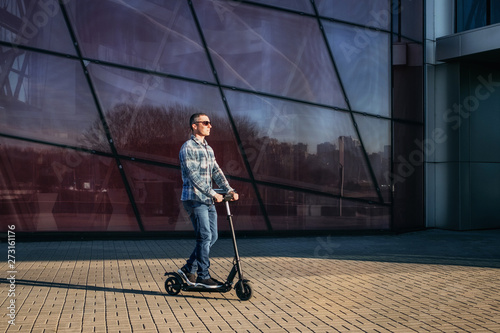 Man riding a electric kick scooter on stone pavement against modern glass wall of building