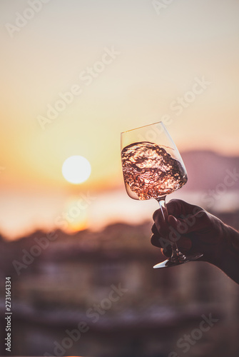 Photography Glass of rose wine in mans hand with sea and sunset at background, close-up