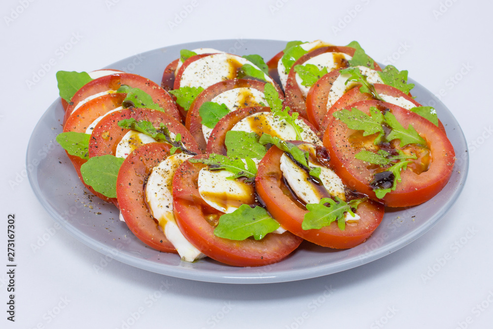 Caprese salad tomatoes mozzarella cheese basil olive oil pepper sauce. Gray plate with caprese on white. Italian cuisine, Mediterranean recipe fresh vegetable salad Caprese salad tomatoes mozzarella cheese basil olive oil pepper sauce. Gray plate with caprese on white. Italian cuisine, Mediterranean recipe fresh vegetable salad