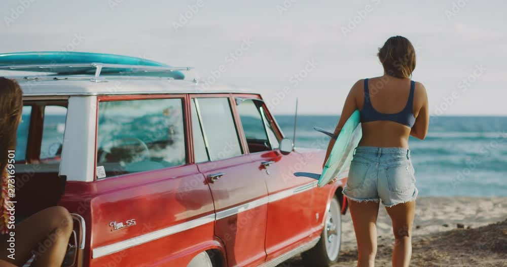 Young attractive women at the beach with vintage beach cruiser car, getting ready to surf at sunset, island beach lifestyle