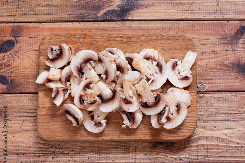 Sliced raw champignon plates on a wooden board, top view
