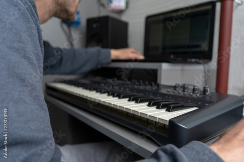 Man recording a song at the home music recording studio. Midi keyboard and a laptop on the table