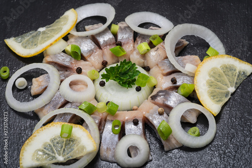 Hollandse Nieuwe- Traditional Dutch Food. Soused raw Herring soaked in mild marinade. Garnished with Lemon, Onion and Parsley on black natural stone. photo