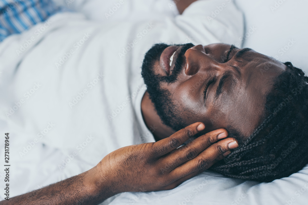 overhead view of african american man suffering from headache in bedroom overhead view of african american man suffering from headache in bedroom