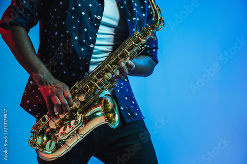 Fotografia Young african-american jazz musician playing the saxophone on blue studio background in trendy neon light