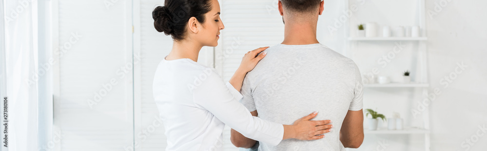 panoramic shot of man sitting on massage table near attractive healer