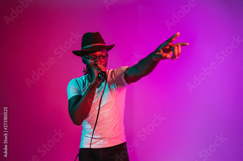 Photography Young african-american jazz musician with microphone singing a song on purple studio background in trendy neon light