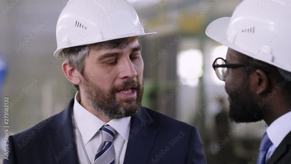 Up-section shot of multi-ethnic managers staying at factory and having conversation
