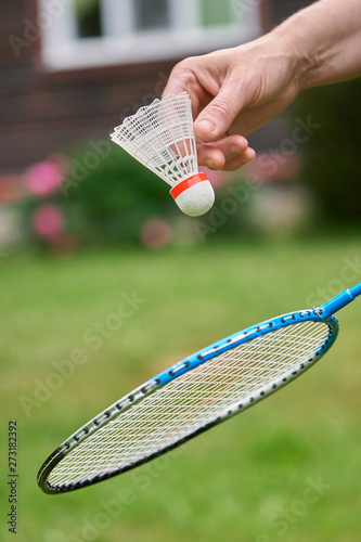 Female hand holds a white badminton shuttlecock and a racket outdoors