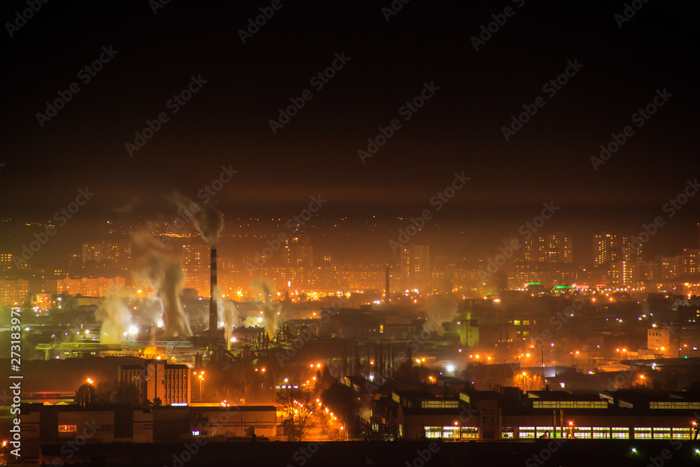 Night city industrial zone. Smoke from the pipes of manufacturing. Residental aeria houses and car traffic lights