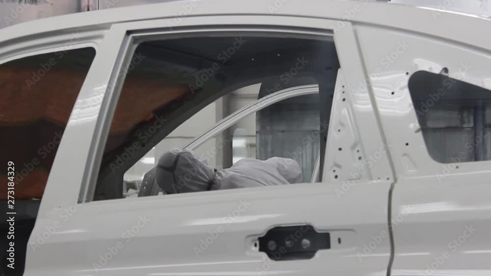 Workers in protective suits and respirators wipe the car body on the conveyor of an automobile plant. Workers in protective suits and respirators wipe the car body on the conveyor of an automobile plant.