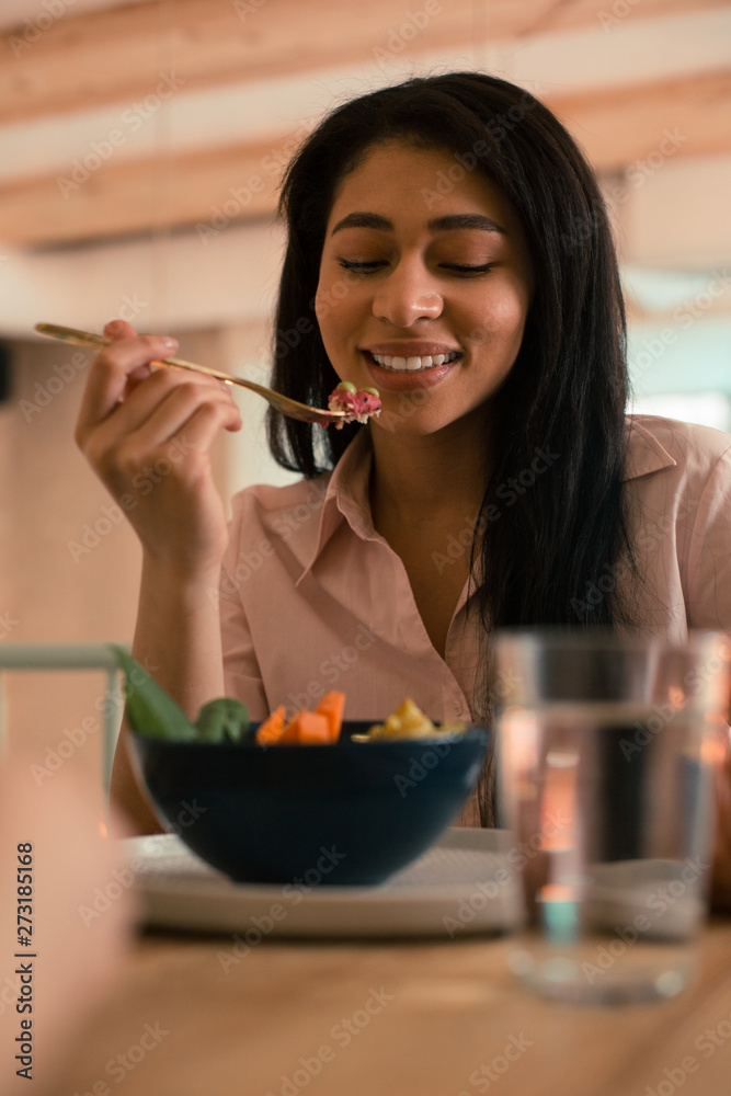 Pleased young lady looking at her fork while eating Pleased young lady looking at her fork while eating