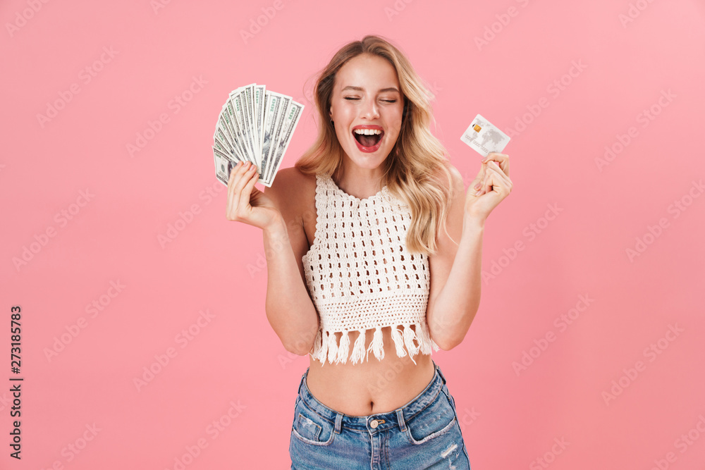 Happy young woman posing isolated over pink wall background holding money and credit card. Happy young woman posing isolated over pink wall background holding money and credit card.