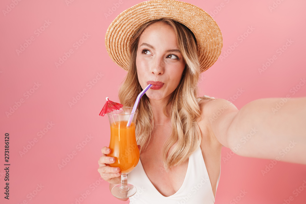 Excited young woman posing isolated over pink wall background dressed in swimwear beach concept drinking cocktail take selfie by camera. Excited young woman posing isolated over pink wall background dressed in swimwear beach concept drinking cocktail take selfie by camera.