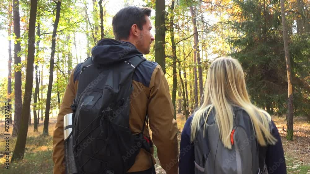 A hiking couple walks down a path through a forest on a sunny day and talks - rear view A hiking couple walks down a path through a forest on a sunny day and talks - rear view