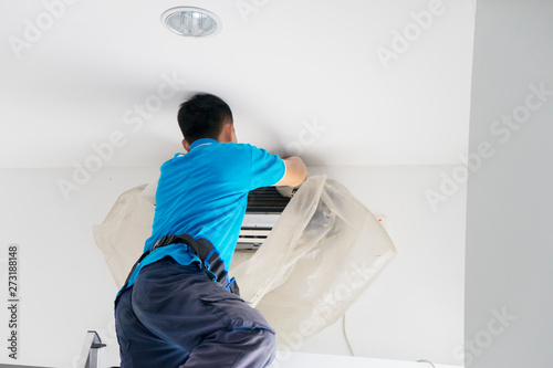 Male worker cleaning an air conditioner from dust