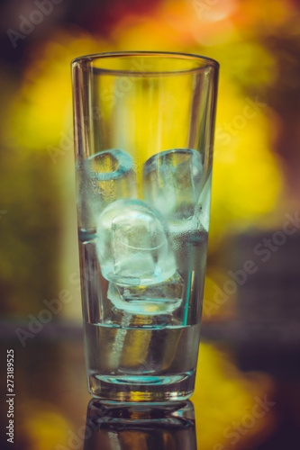Empty glass with ice cubes in it sitting on a table at a bar or restaurant – Elegant recipient for refreshing drinks in summer on a mirror surface with reflection